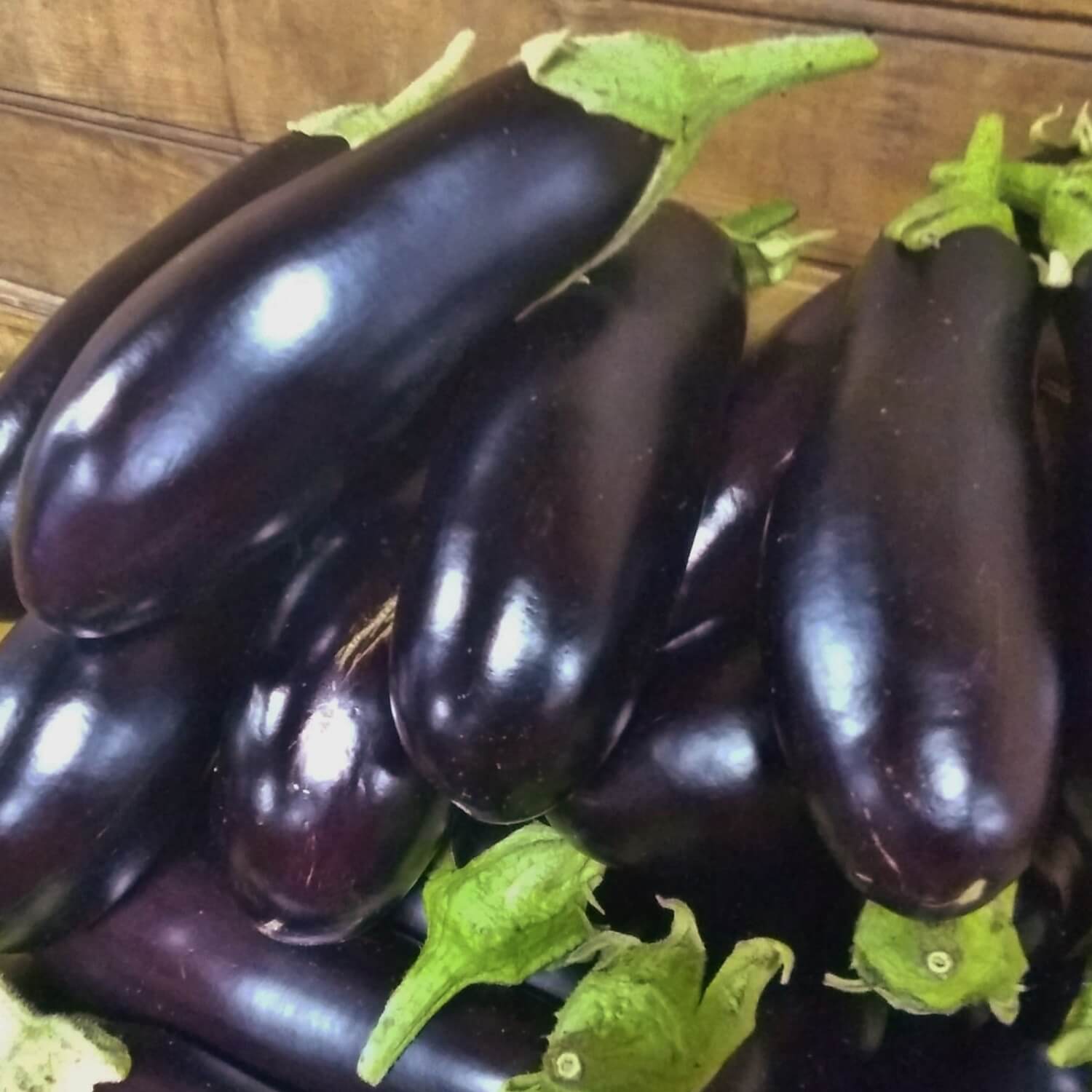 Bunch of dark purple diamond eggplants with green stems on a wooden surface