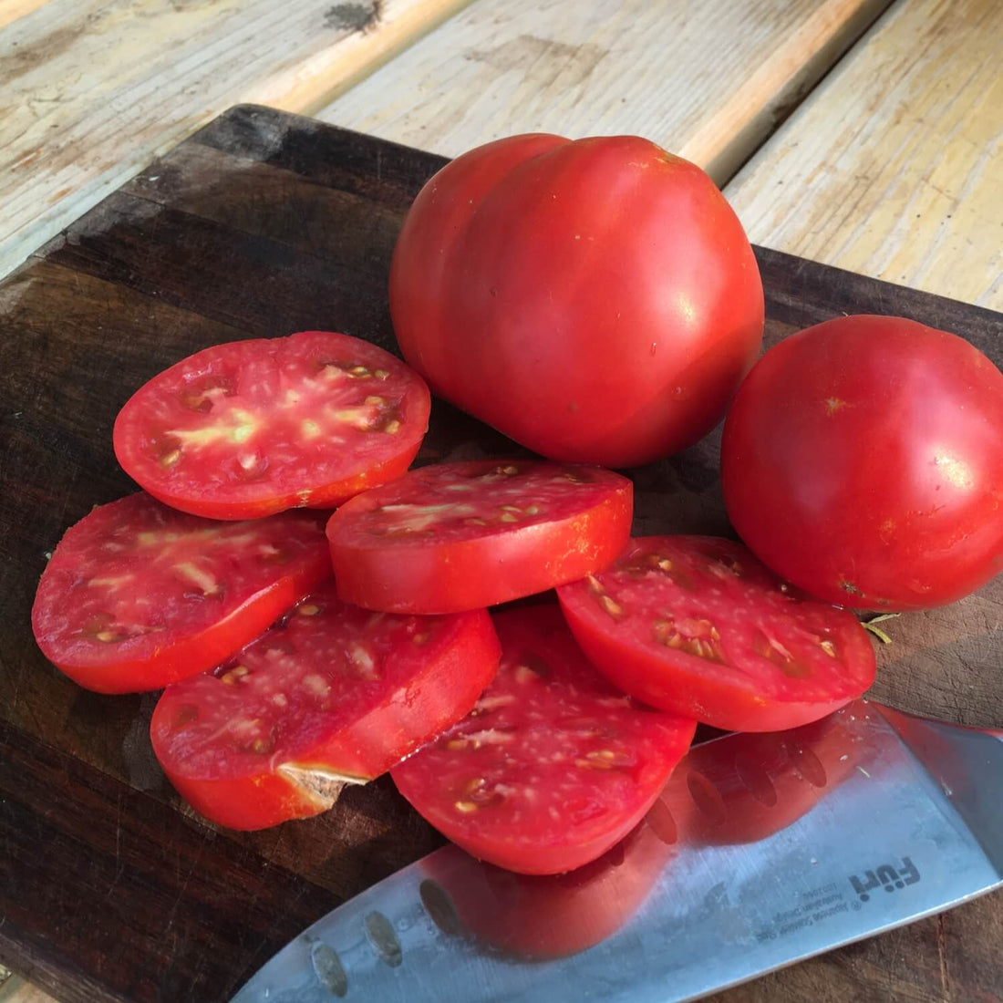 Sliced and whole Cosmonaut volcav tomatoes on a wooden cutting board with a knife.