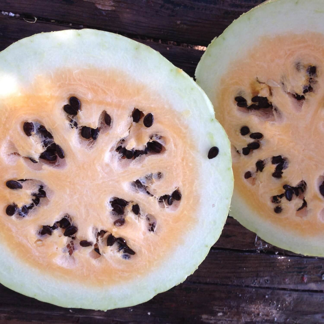 Two halves of a Desert king watermelon with seeds on a wooden surface