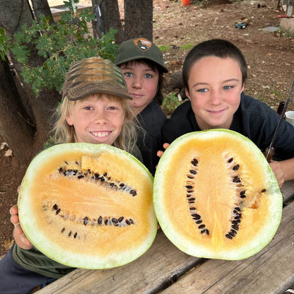 Three children holding a halved watermelon outdoors.