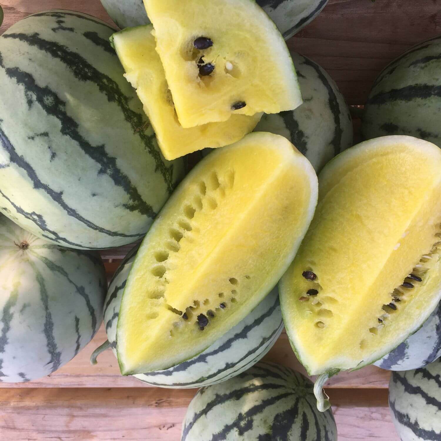 Halved watermelons with yellow flesh and dark green rind on a wooden surface.