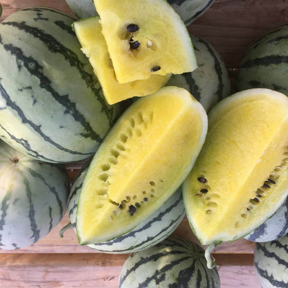 Halved watermelons with yellow flesh and dark green rind on a wooden surface.