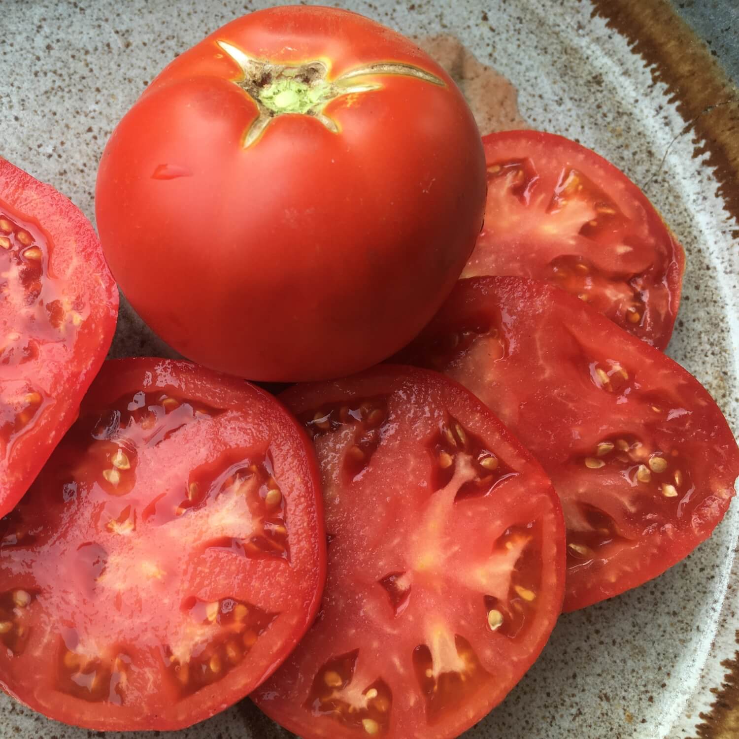 Whole and sliced red Thessaloniki tomatoes on a textured surface