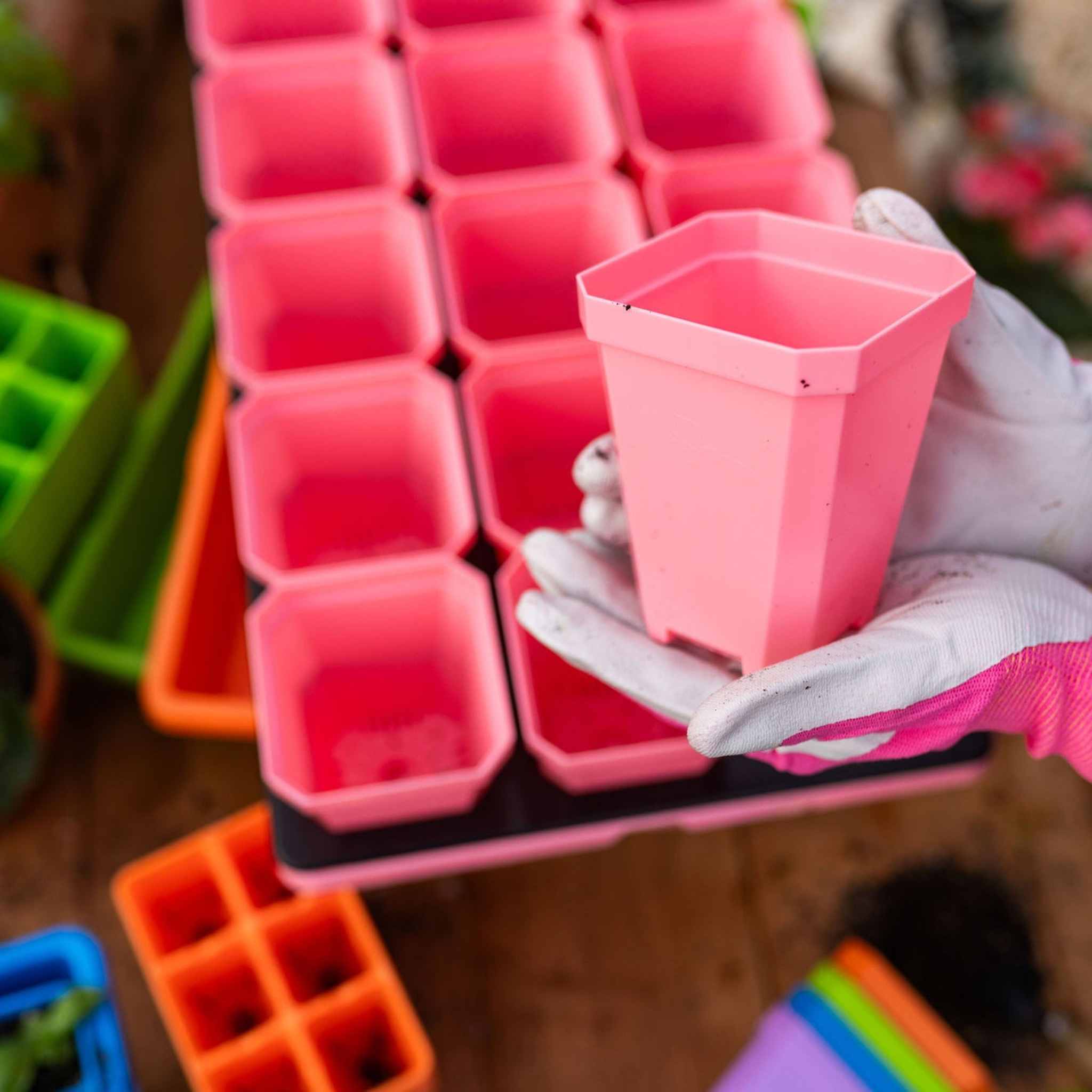 Person holding a pink pot with a tray of pink seedling trays in the background 