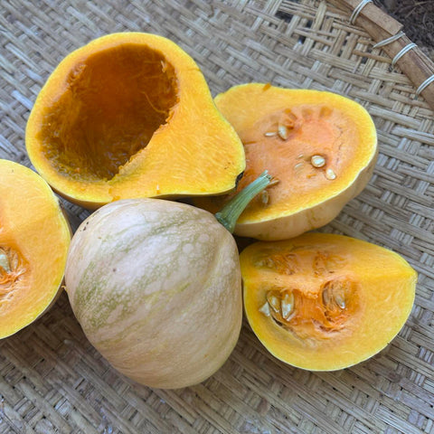 Sliced and whole yellow seminole pumpkins on a woven surface