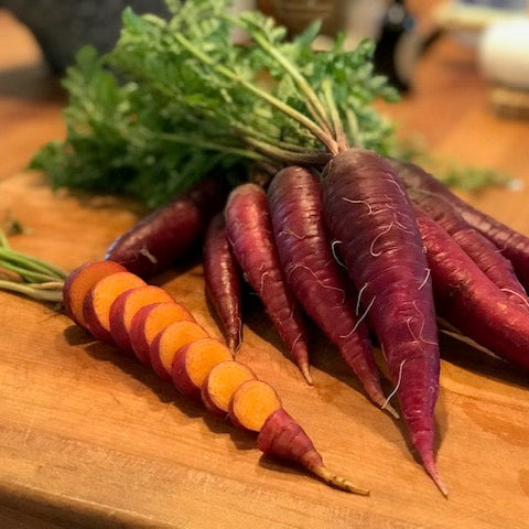 A bunch of purple-skinned carrots with an orange core, freshly harvested and placed on a wooden cutting board.